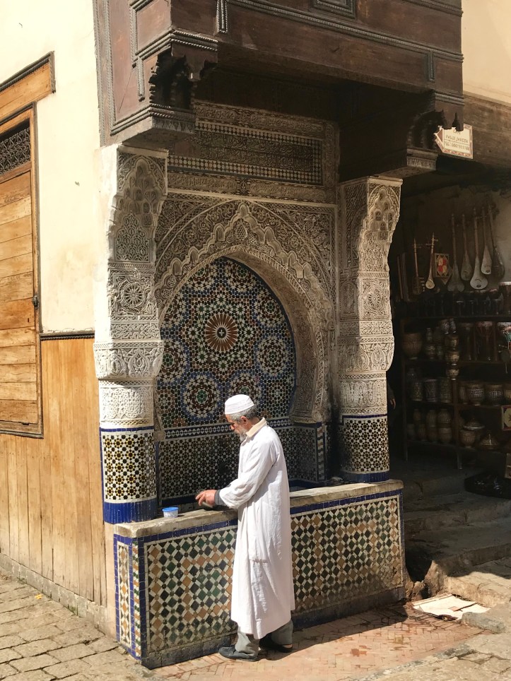 Uomo vestito di bianco davanti a una fontana nella medina di Fes, Marocco