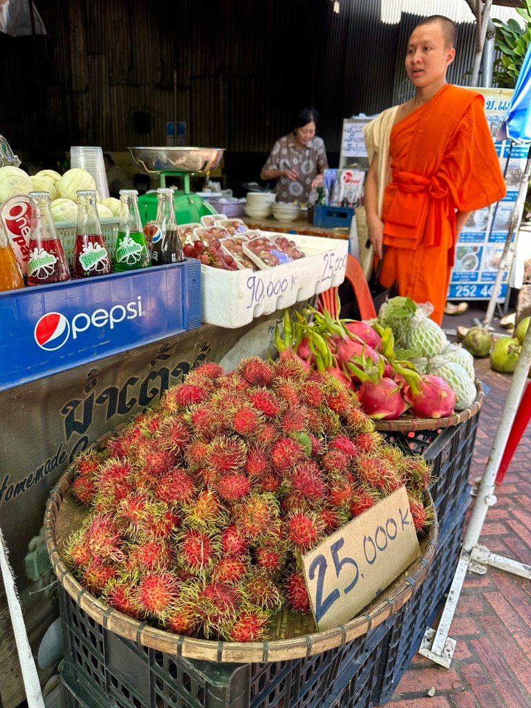 Monaco buddista vestito di arancione, fermo ad una bancarella di frutta a Luang Prabang, Laos 
